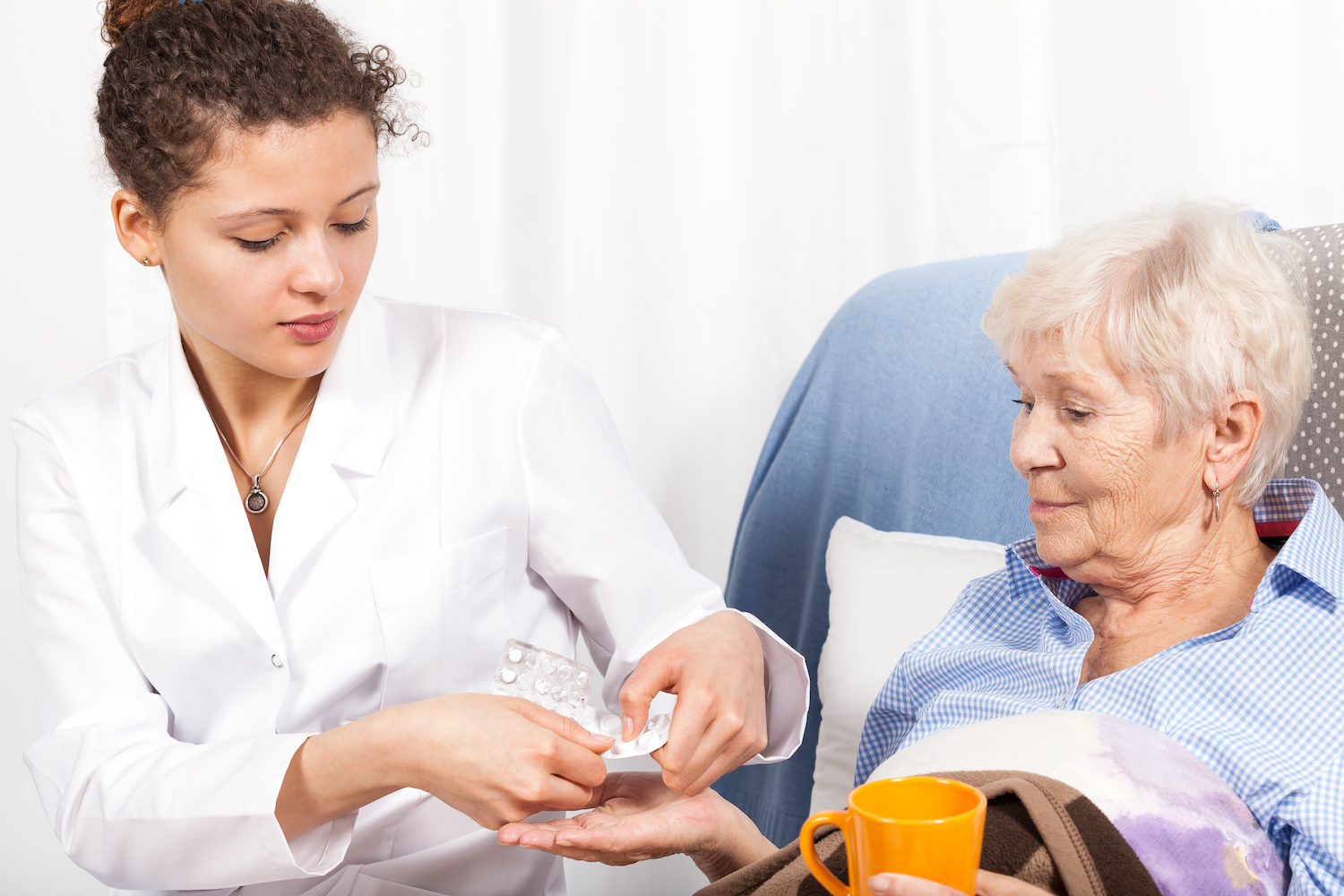 Home nurse giving elderly woman vitamin